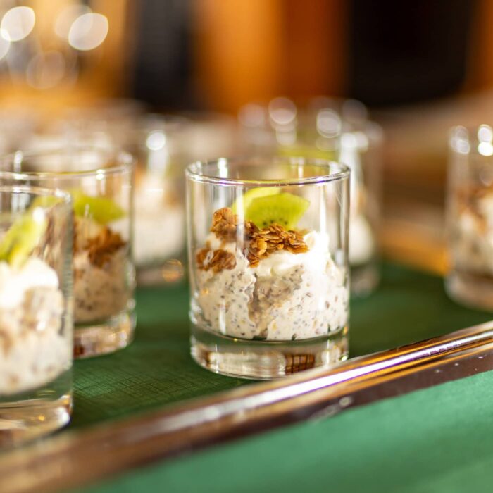 Kleine Gläser mit einer Schicht aus cremigem Dessert, garniert mit püriertem Obst und knusprigen Nüssen, auf einem Tablett präsentiert. Ideal für elegante Veranstaltungen und Catering.