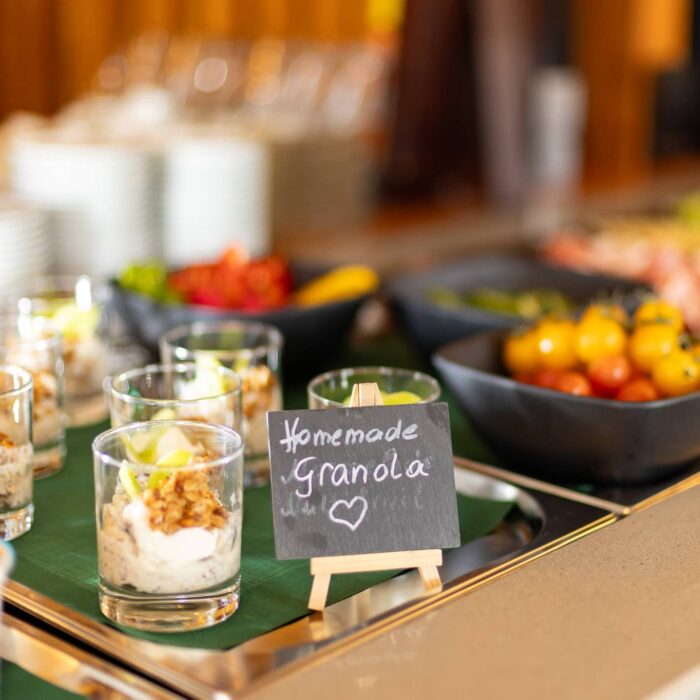 Buffet mit frischen Speisen, darunter Gläser mit selbstgemachter Granola und frischem Obst, präsentiert auf einem eleganten Tisch.