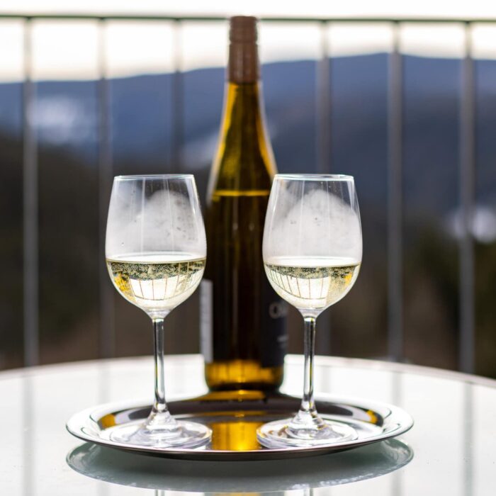 Zwei Gläser mit sprudelndem Weißwein auf einem silbernen Tablett, im Hintergrund eine Flasche Weißwein und eine malerische Berglandschaft. Ideal für romantische Anlässe oder festliche Feiern.