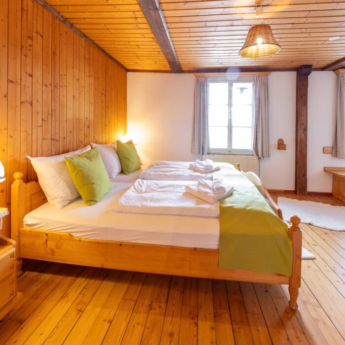 Helles und gemütliches Schlafzimmer mit zwei Betten, Holzwänden und einem warmen Ambiente. Die Bettwäsche ist in Weiß und Grün gehalten, und ein Fenster sorgt für natürliche Beleuchtung. Ideal für einen erholsamen Aufenthalt in einer ländlichen Unterkunft.