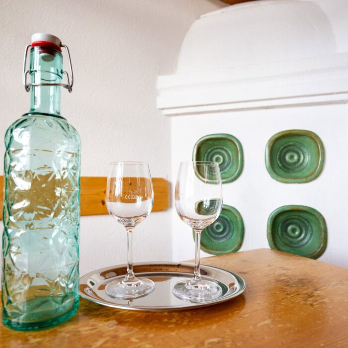 Glasflasche mit Verschluss neben zwei Gläsern auf einem Tablett, vor einem weißen Hintergrund mit grünen Details. Ideal für stilvolle Tischdekoration oder als Inspiration für Getränkepräsentationen.