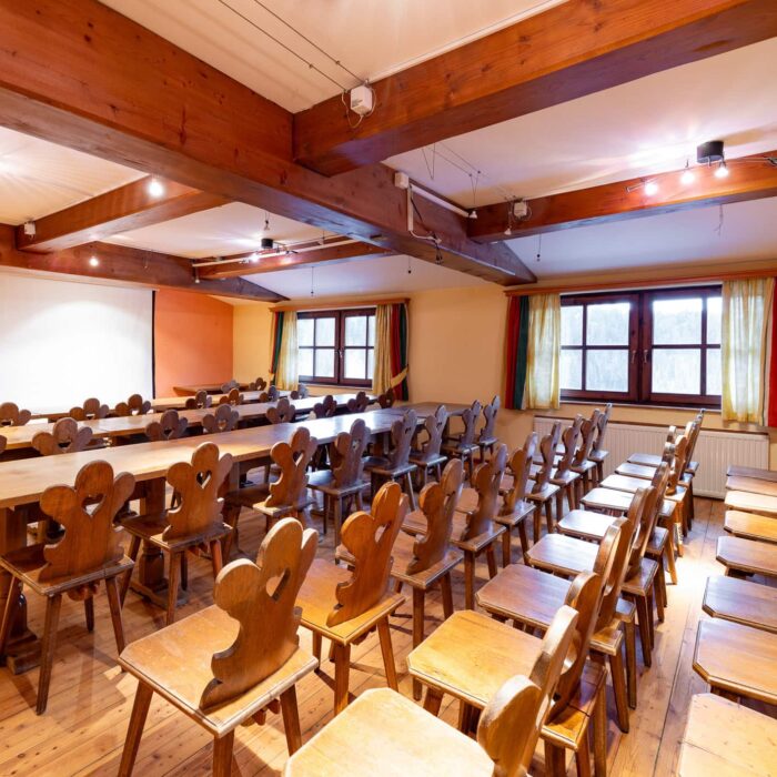 Innenansicht eines Seminarraums mit Holzstühlen und Tischen, ideal für Workshops oder Schulungen. Die warmen Farben und das natürliche Licht schaffen eine einladende Atmosphäre.