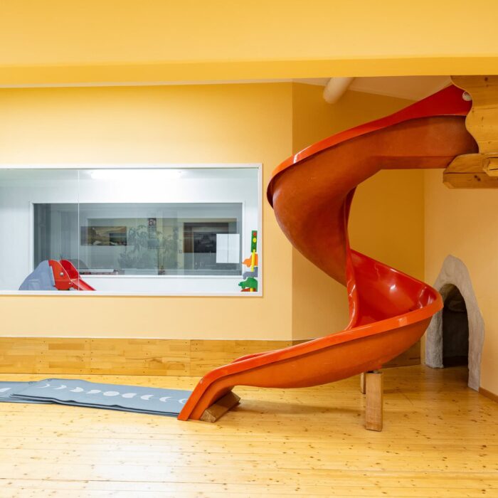 Rote Rutsche in einem hellen Spielbereich mit Spiegel im Hintergrund, ideal für Kinder zum Spielen und Entdecken.