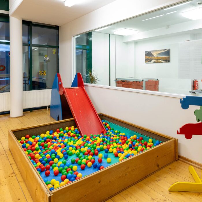 Bunte Spielplatzlandschaft mit einer großen Kiste voller Kunststoffbälle und einer roten Rutsche, ideal für Kinder zum Spielen und Entdecken in einem modernen Innenraum.