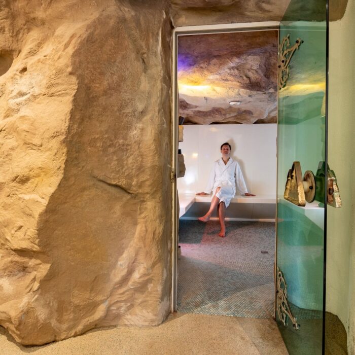 Entspannender Wellnessbereich mit natürlichem Felsdesign, ein Mann in einem Bademantel sitzt in einem modernen Raum mit sanfter Beleuchtung. Ideal für Spa- und Erholungsangebote.