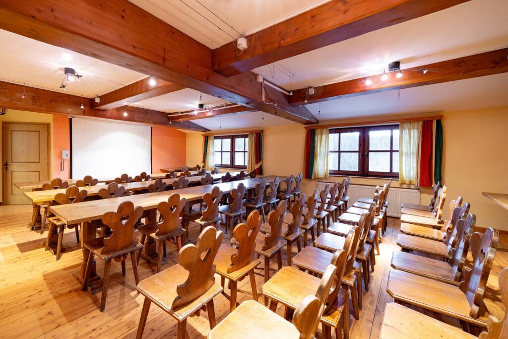 Innenansicht eines Seminarraums mit Holzstühlen und Tischen, ideal für Schulungen oder Workshops, natürliche Beleuchtung durch große Fenster.