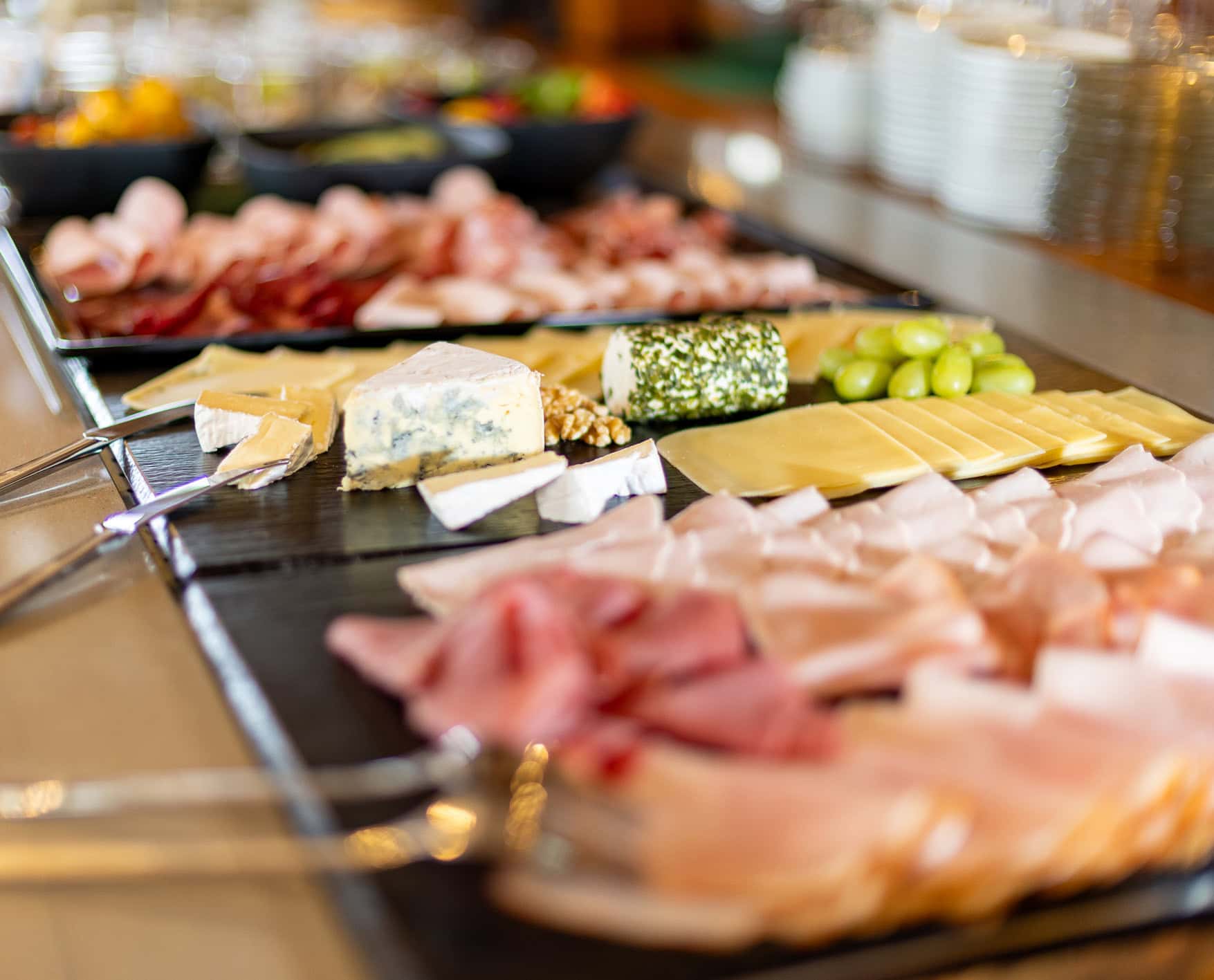 Bunte Auswahl an Wurst- und Käseplatten auf einem Buffet, mit verschiedenen Sorten von Schinken, Salami, Käse und frischem Obst, ideal für Feiern oder Veranstaltungen.