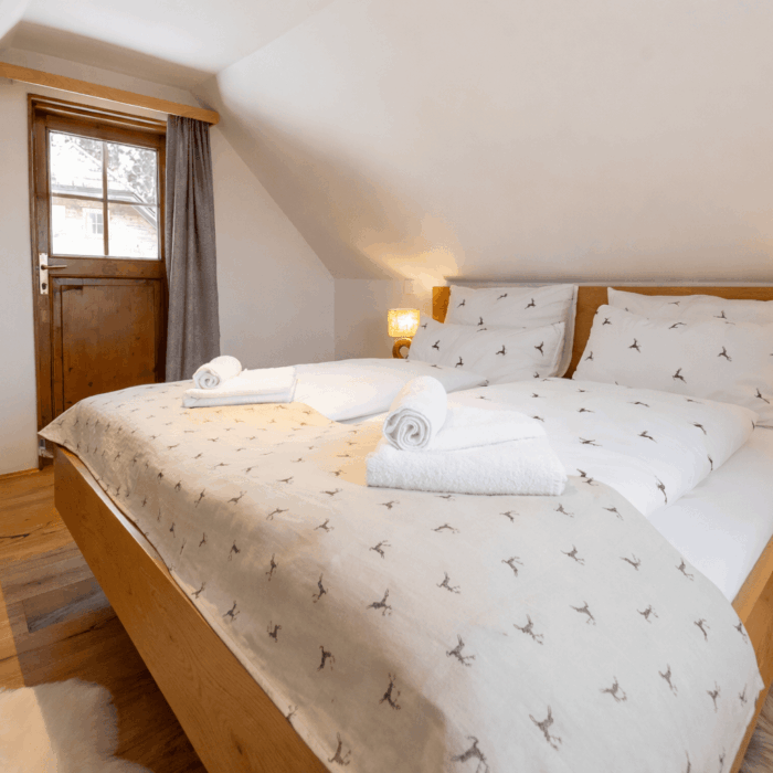 Gemütliches Schlafzimmer mit Doppelbett, frisch bezogenen Betten und Handtüchern, hellen Wänden und einem Fenster, das natürliches Licht hereinlässt. Ideal für einen entspannten Aufenthalt.