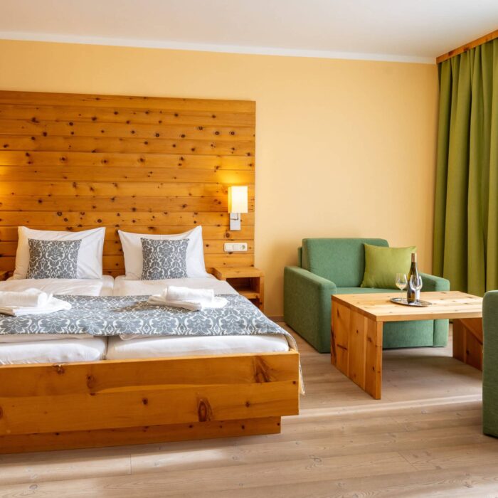 Helles und modernes Hotelzimmer mit Doppelbett, gemütlicher Sitzecke und Holzdetails, ideal für einen entspannten Aufenthalt.