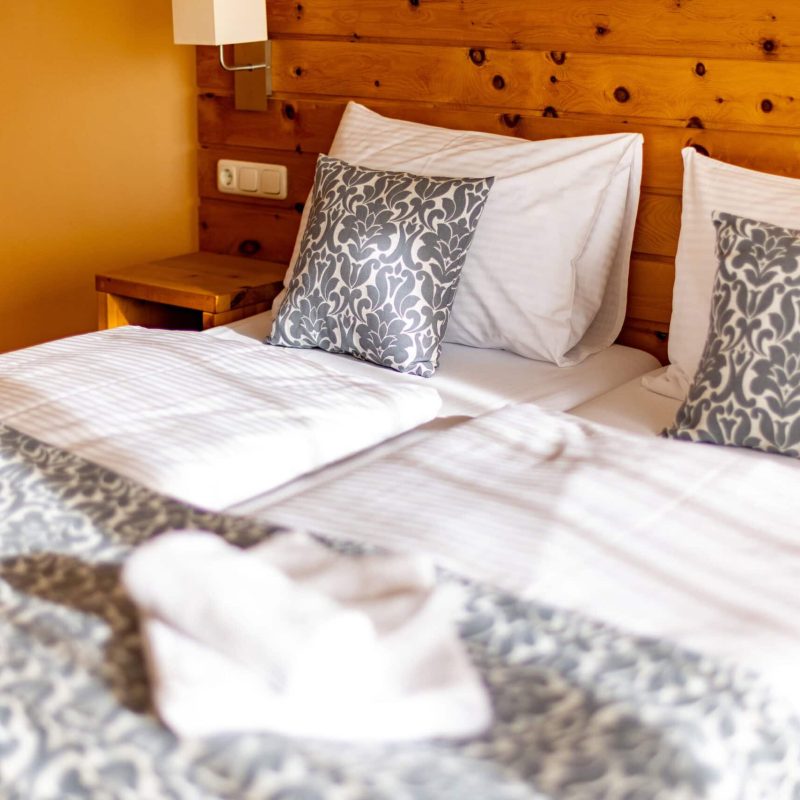 Gemütliches Schlafzimmer mit zwei Einzelbetten, dekoriert mit eleganten Kissen und einer stilvollen Tagesdecke. Die Wände aus Holz verleihen dem Raum eine warme Atmosphäre, ideal für entspannte Nächte.